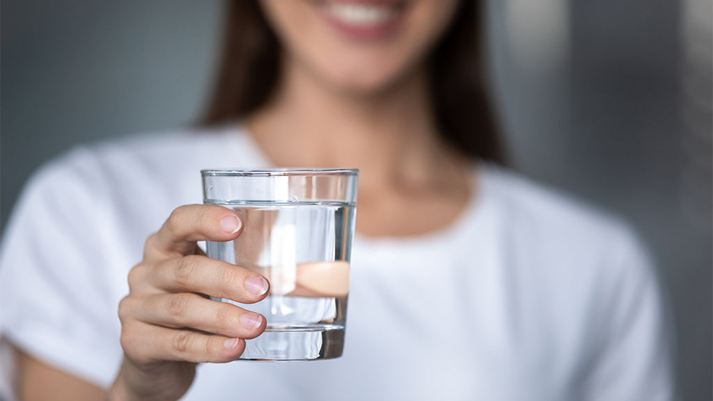 Muskeln: Frau zeigt ein Glas mit Wasser