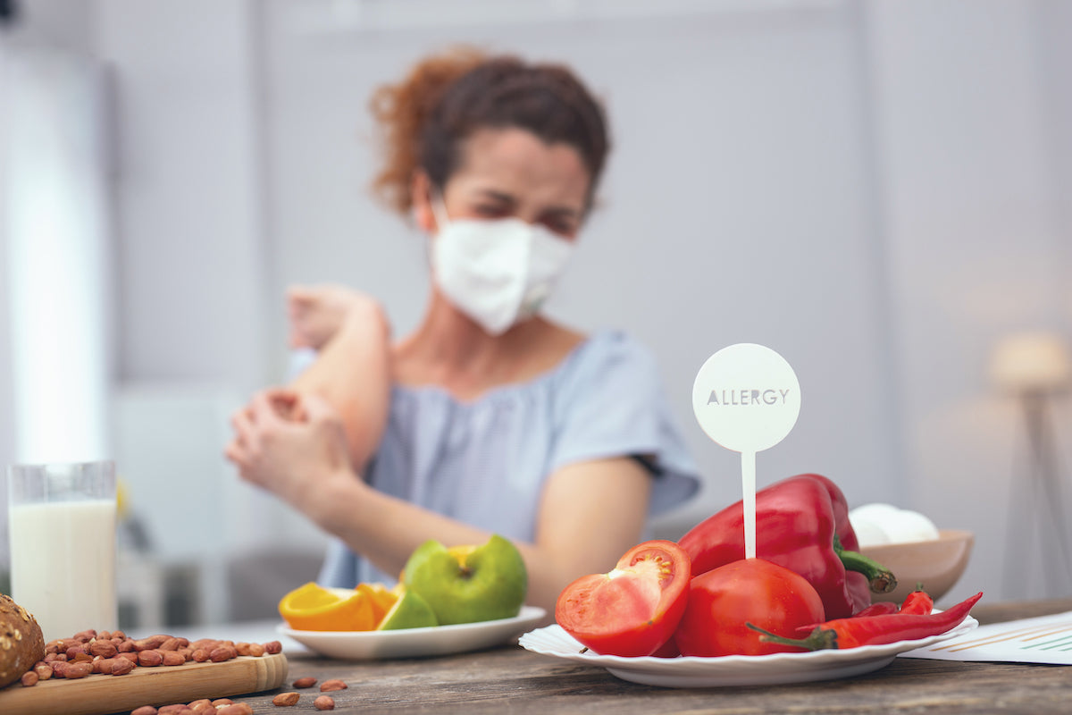 Frau mit Maske kratzt sich wegen Allergie gegen Gemüse am Arm