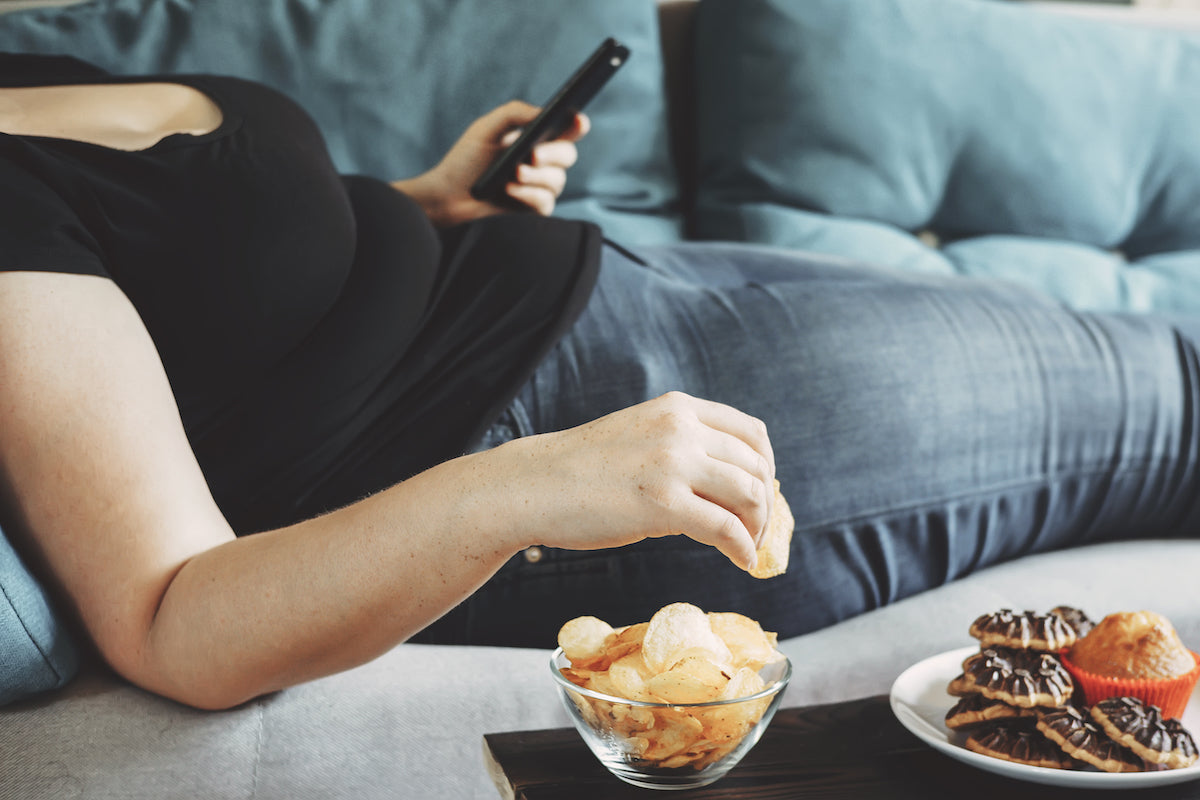 Person liegt mit Fernbedienung und Snacks auf dem Sofa
