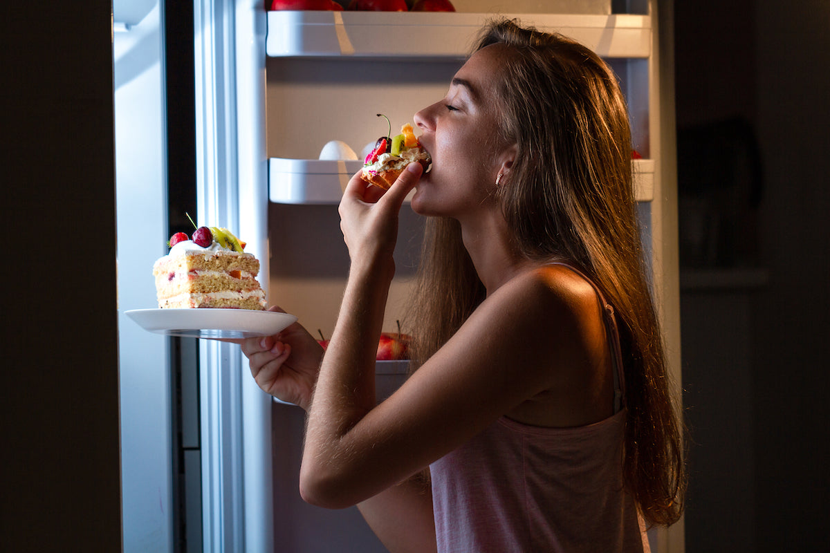 Eine Frau isst Torte mit offener Kühlschranktür