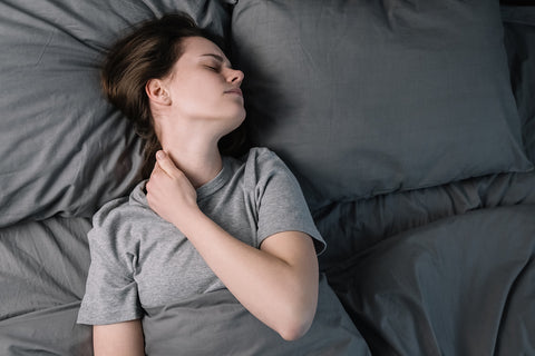 Frau liegt im Bett und greift sich vor Schmerzen an den Nacken