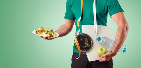 Mann hält Salat, Waage, Apfel, Wasserflasche und Maßband