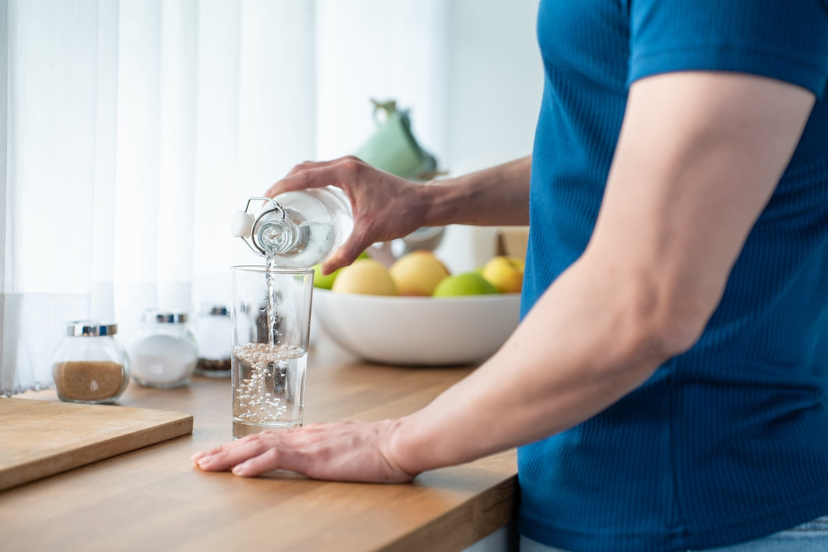 Person schenkt sich ein Glas Wasser ein